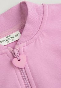 Różowy materiał bluzy z gładką teksturą, z zamkiem na suwak w kształcie serca i ściągaczem przy kołnierzu. Metka wskazuje rozmiar 6Y, marka Coccodrillo.