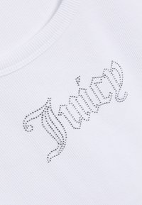 Λευκό ριμπ ύφασμα με τη λέξη "Timothy" γραμμένη με μικρές ασημένιες στρας σε στυλιζαρισμένη καλλιγραφική γραμματοσειρά.