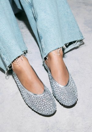 Sølv slip-on sko dækket med rhinsten, med en glat tekstur og rund tå; parret med lyseblå slidte denimbukser.