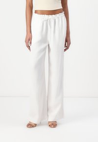 Pantaloni bianchi a gamba larga con vita elasticizzata, realizzati in tessuto leggero, dalla texture liscia e dal fit rilassato. Abbinati a sandali beige.