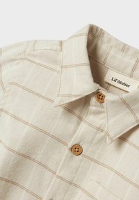 Beige rutete skjorte med brune striper, laget av bomull, med krage og treknapper. Merket leser "Lil'Atelier."