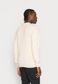 Lys beige genser med lange ermer, myk tekstur, og ribbet mansjett og kant. Vist fra baksiden, kombinert med mørke bukser.