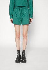 Shorts verdes con cintura elástica y cordón, con un patrón texturizado. Combinados con botas negras hasta el tobillo.