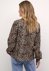 Halenka s leopardím potiskem vyrobená z lehké látky, s dlouhými rukávy, volným střihem a zakřiveným lemem. Vyznačuje se výrazným vzorem v černé, hnědé a béžové barvě.