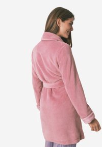 Jasnoróżowy szlafrok z polaru z długimi rękawami, kołnierzykiem, paskiem w talii i teksturowanymi mankietami. Gładki, przytulny materiał w jednolitym kolorze.