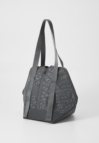 Grå tote bag med et geometrisk mønster, glidelåslukking og to stoffhåndtak. Laget av polypropylen med en strukturert overflate og vinklet form.