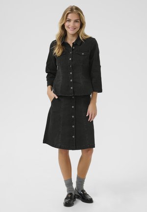 Veste en denim noir avec deux poches poitrine et jupe assortie arrivant au genou, présentant des fermetures à bouton et des détails de couture contrastés.