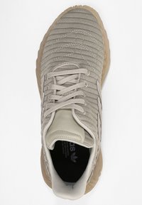 Ljust beige atletiska skor med texturerad stickad ovandel, läderdetaljer och robust gummisula. Har flexibel snörning och vadderad krage.