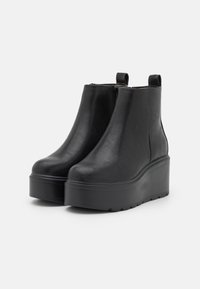Stivaletti neri realizzati in morbida pelle sintetica con suola platform a zeppa. Presentano un’etichetta sul retro per una facile calzata e una chiusura con cerniera sul lato.