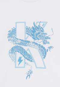 T-shirt blanc avec un graphisme de dragon bleu s'entrelacent avec un "K" stylisé et un éclair, ajoutant de l'intérêt visuel au design.
