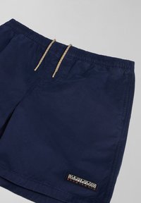 Navy blue swim shorts made of lightweight fabric, featuring an elastic waistband with a beige drawstring and a logo patch on the side.