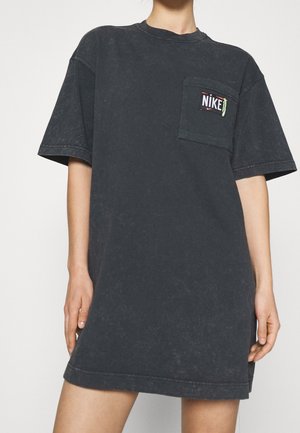 Robe t-shirt noire oversize en coton, dotée d'une poche avant avec un logo Nike multicolore. Texture douce avec un style vintage.