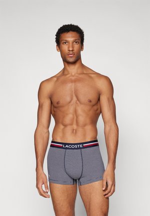 Herren Boxer Shorts in Marineblau mit weißen Streifen, ausgestattet mit einem schwarzen Bund, der mit roten und weißen Akzenten sowie dem Lacoste-Logo verziert ist.