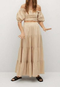 Kaksiosainen asu, johon kuuluu vaaleanbeige lyhythihainen toppi puff-hihoilla ja kerroksellinen maksihame, molemmat pehmeää puuvillakangasta. Korostettuna elastisella vyötäröllä.