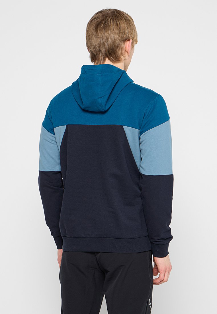 Felpa con cappuccio caratterizzata da un design a blocchi di colore blu e blu navy, con una texture morbida e polsini elasticizzati. La vista posteriore mostra pannelli a contrasto.