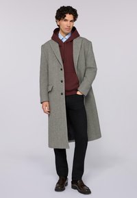 Grå ullrock med kantslag, svarta knappar, lager på lager över en vinröd hoodie och ljusblå skjorta, tillsammans med svarta byxor och bruna skor.