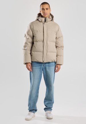 Chaqueta de plumas цвет завоевать con capucha, con un diseño acolchado y cierre de botones. Llevada sobre jeans celestes y zapatillas blancas.
