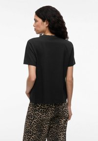 T-shirt nera a maniche corte con scollo rotondo, caratterizzata da una vestibilità rilassata. Il modello indossa pantaloni larghi con stampa leopardata.