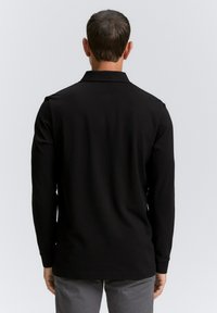 Camisa polo negra de manga larga hecha de una tela suave, con un cuello y detalles de botones en el cuello. Ajuste simple y estructurado.