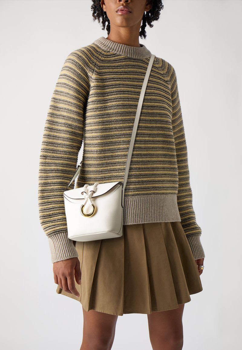 Stripet strikkegenser med rund hals, kombinert med et plisserte olivengrønt skjørt. En liten hvit skinnveske med gullhardware bæres som crossbody.