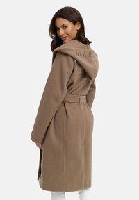 Manteau en mélange de laine marron avec une grande capuche, taille ceinturée et tissu texturé. "MARK." est brodé sur la capuche dans une couleur assortie.