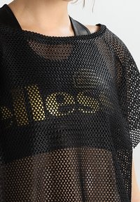 Top in rete nero con una vestibilità ampia, dotato di un logo dorato "ellesse". Il tessuto presenta un motivo a diamante ed è semi-trasparente.
