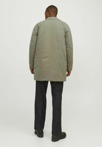 Abrigo acolchado largo en gris claro con una silueta estilizada y un cuello con muescas. Lleva pantalones negros y botas de tobillo.
