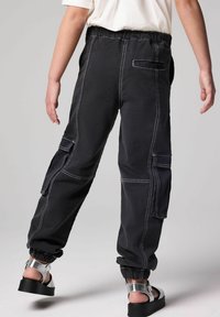 Mustat cargo-housut, joissa on joustava vyötärö, valkoiset tikkaukset, useita taskuja ja kapenevat lahkeet. Yhdistetty hopeaketjusaappaiden kanssa.