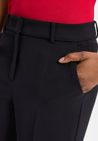 Zwarte op maat gemaakte broek met een soepele textuur, een platte voorkant, zijzakken en een riemlus. Draagt met een rode aansluitende top.