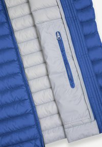 Modrá a světle šedá prošívaná bunda se svislým zapínáním na zip na vnitřní kapse a viditelnými švy podél panelů látky.