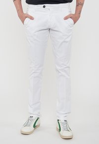 Chinos bianchi in cotone con un fit slim, dotati di tasche laterali, chiusura con un singolo bottone, abbinati a sneaker bianche con dettagli verdi.