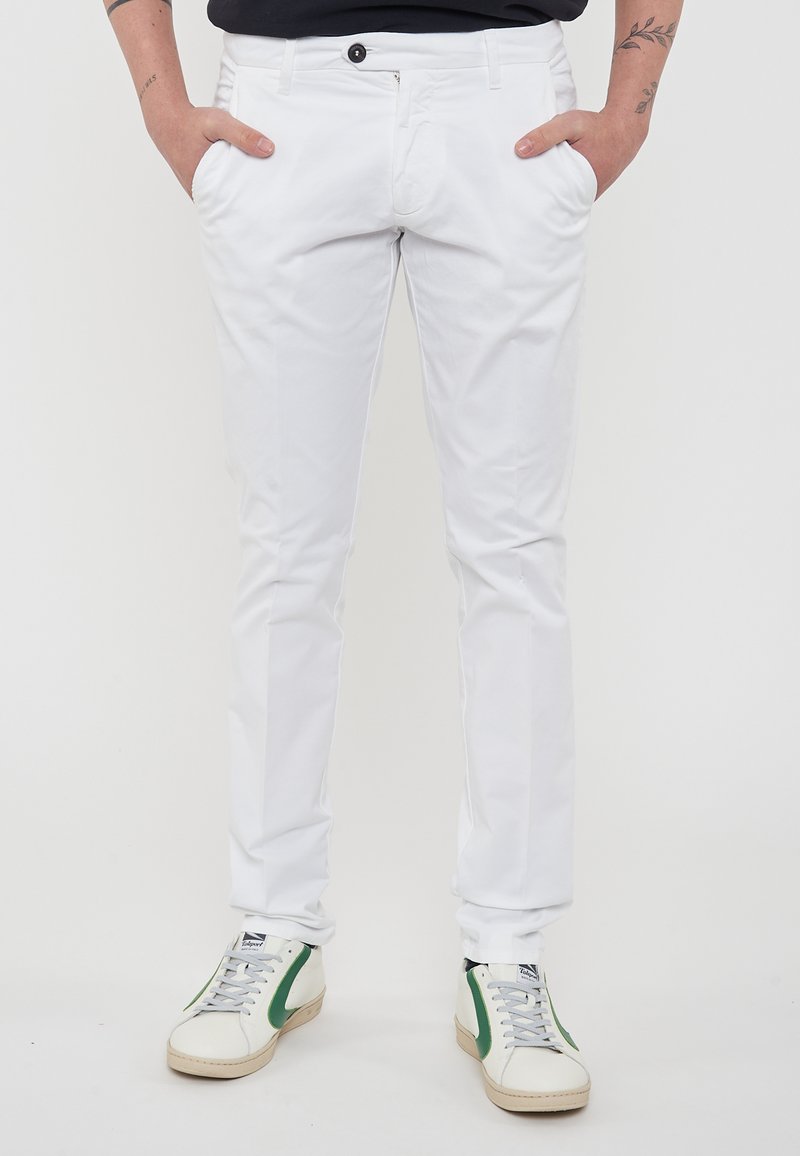 Chinos bianchi in cotone con un fit slim, dotati di tasche laterali, chiusura con un singolo bottone, abbinati a sneaker bianche con dettagli verdi.