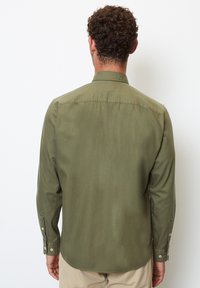 Olivově zelená košile s dlouhým rukávem vyrobená z hladkého materiálu, s límcem na knoflíky a knoflíkovými manžetami, s standartním střihem a detailem na zadní části.