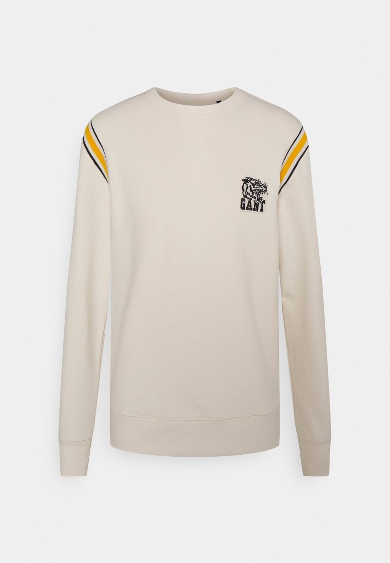 Sweat-shirt beige à manches longues avec des rayures jaunes et noires sur les épaules, col rond, et logo tigre avec le texte "GANT" sur la poitrine.