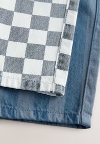 Dve vzorčni tkanini: ena s črno-belim karo vzorcem, druga v enobarvnem svetlo modrem jeansu. Obe imata gladko teksturo.