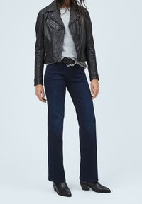 Černá kožená motorkářská bunda, šedý svetr, tmavě modré zvonové džíny a černé kotníkové boty na podpatku. Jednoduchý pásek.