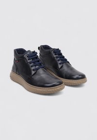 Zapatillas altas de cuero color navy con cordones azules, suela de goma en beige y acabado texturizado, con detalles de costura sutil.