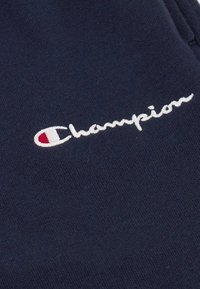 Marineblauer Baumwoll-Sweatshirt mit weißem, gesticktem "Champion"-Logo und einem kleinen roten Akzent im Buchstaben "C". Glatte Textur.