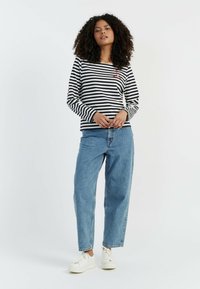 Langärmliges gestreiftes Oberteil in Navy und Weiß, mit einem kleinen roten Logo auf der Brust, kombiniert mit hochgeschnittenen hellblauen Jeans und weißen Sneakern.