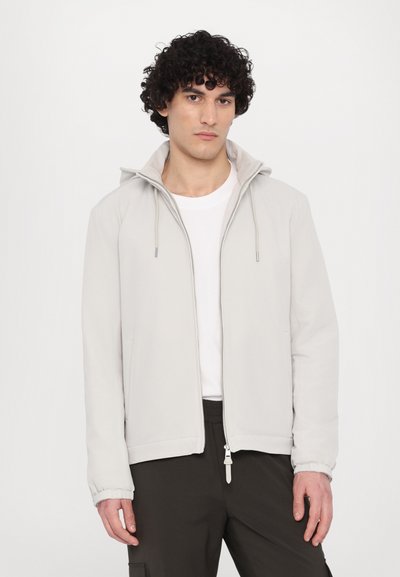 Hele halli kapuutsiga zip-up jope, elastsete mansettide ja nööridega. Kandmisel valge T-särgi peal, koos tumedate pükstega. Lihtne disain.