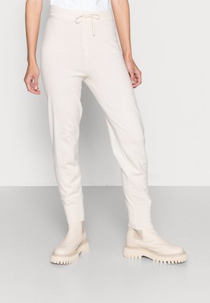 Calças de jogging creme com cintura com cordão, ajuste slim e textura suave, combinadas com botas de tornozelo bege chunky com solas texturizadas.