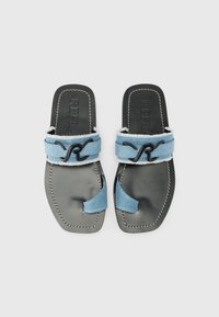Flat sandals with grey leather soles and blue denim straps, featuring a curved cutout and contrasting black hardware accents.
