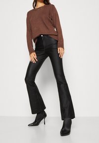 Pull marron à manches longues avec poignets côtelés, associé à un pantalon noir évasé et des bottes à talons hauts pointues noires. Texture douce, design élégant.