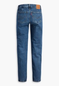 Jeans en denim bleu vus de dos avec deux poches arrière, passants de ceinture et une étiquette de marque en cuir beige sur la taille.