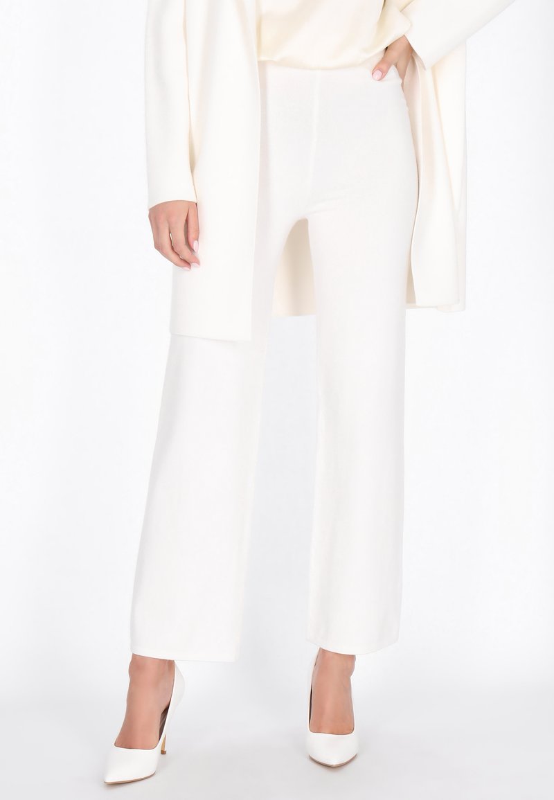 Witte, wijde gebreide broek met een gladde textuur, gecombineerd met een bijpassend licht gekleurd top en witte puntige hakken.