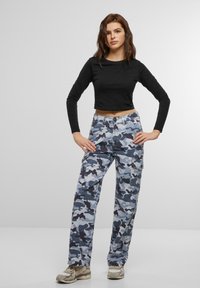 Top corto de manga larga negro combinado con pantalones cargo camuflados en azul y gris, con bolsillos laterales y un corte relajado. Calzado: zapatillas beige.