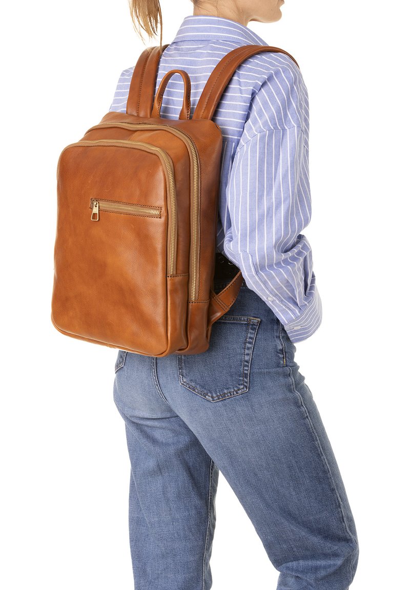 Zaino in pelle marrone con due scomparti, tasca frontale con zip e spallacci, esposto su una camicia a righe e jeans.