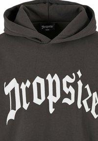 Grå hettegenser med snor, med stor hvit gotisk skrift "Dropsie." Stoffet ser mykt ut med en jevn tekstur. Størrelse merket inni.