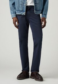 Navyblå chinos i bomull med rak skärning och sidofickor, i kombination med en ljus denimjacka och bruna läderstövlar.