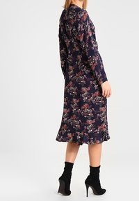 Marineblaues Blumenkleid mit langen Ärmeln, gerafftem Saum und taillierter Silhouette. Es zeigt Gruppen von bunten Blumenmustern.